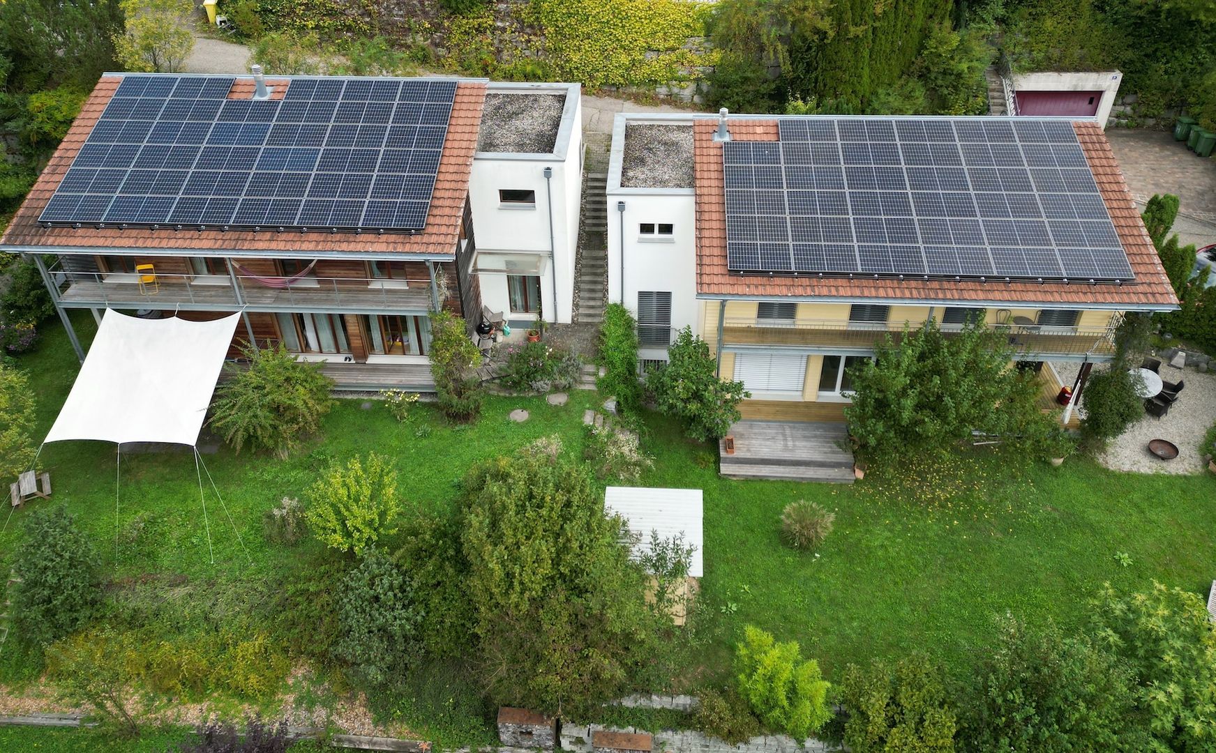 Eine Luftaufnahme zeigt zwei Familienhäuser mit grünem Garten, welche eine Photovoltaik-Anlage auf dem Dach haben.